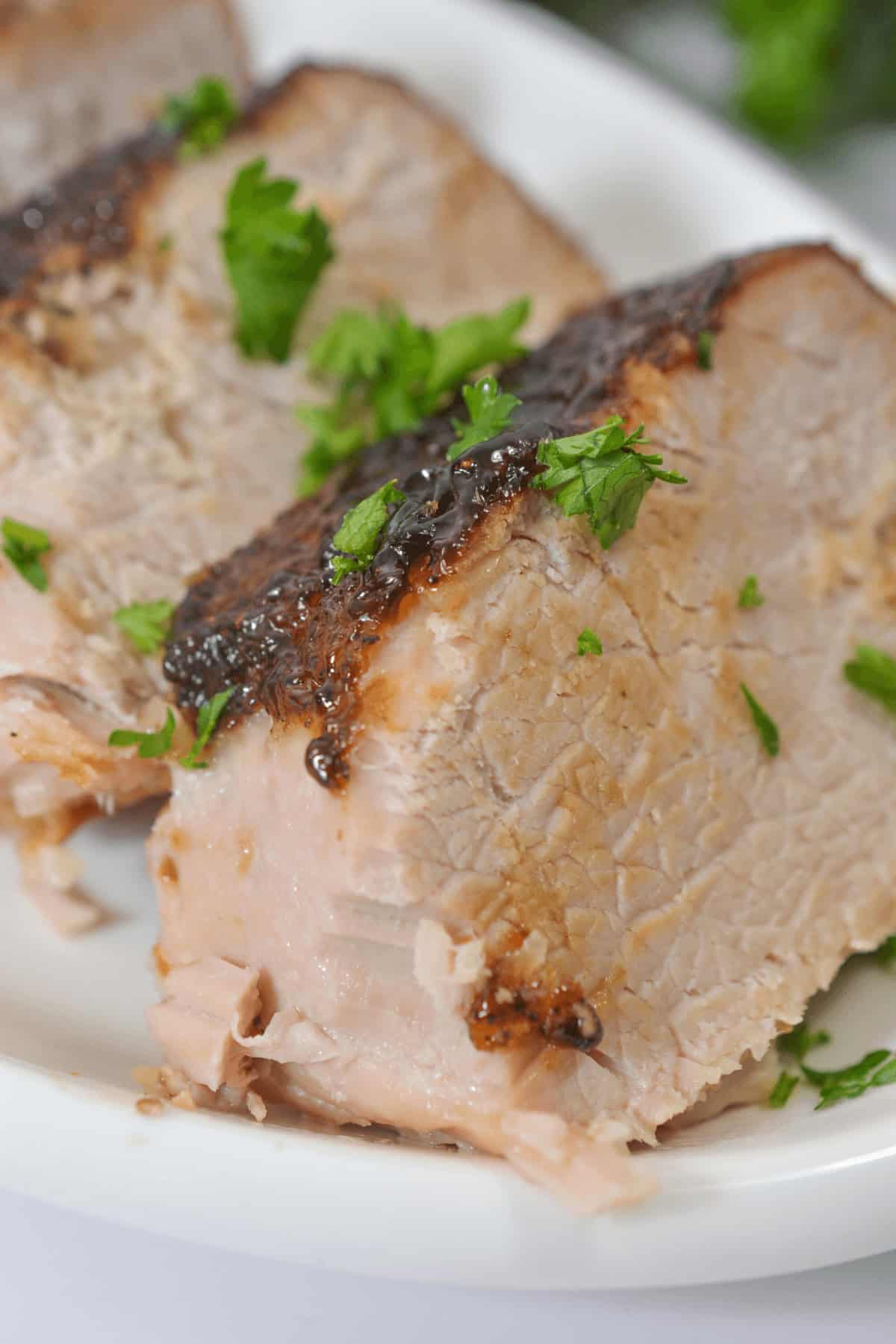 Tender slices of pork with crispy skin, beautifully garnished with fresh parsley on a white plate, evoke the rich flavors of a slow-cooked dish reminiscent of pork tenderloin in a crock pot.
