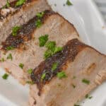 Sliced meat with chopped parsley on a white plate.