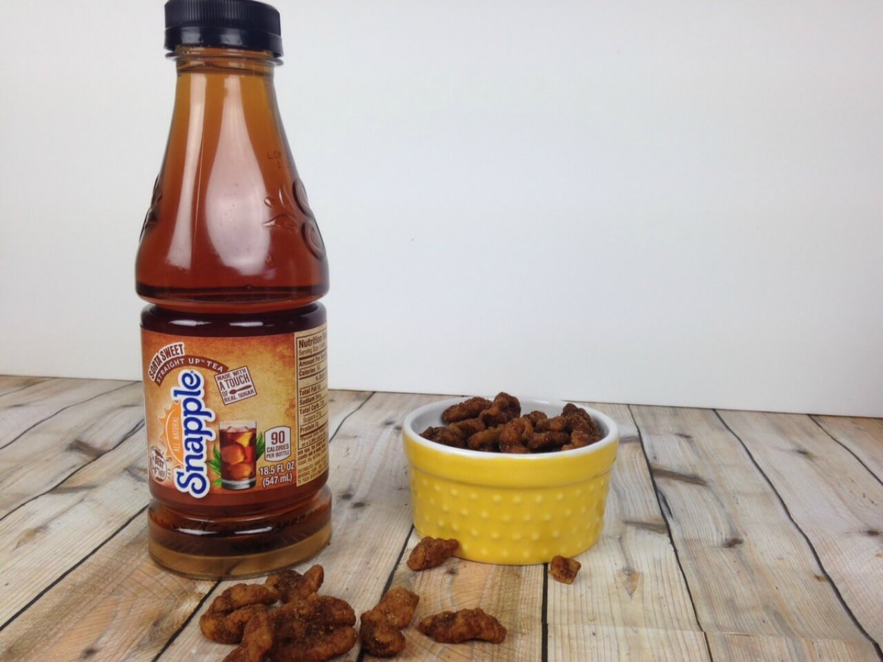 Pumpkin Pie Spiced Walnuts in a small yellow bowl next to a bottle of Snapple Sorta Sweet Tea