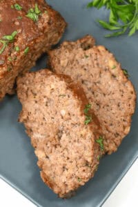 Close-up of bbq meatloaf garnished with herbs, served on a gray plate.