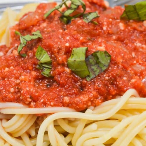 A plate of cooked spaghetti topped with hearty marinara sauce and garnished with chopped fresh basil leaves.