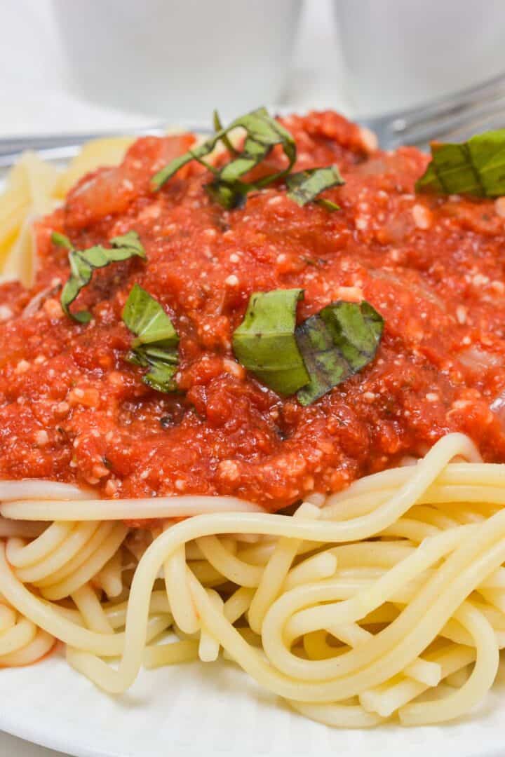 A plate of cooked spaghetti topped with hearty marinara sauce and garnished with chopped fresh basil leaves.