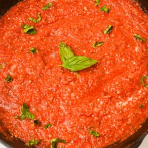 A close-up of hearty Marinara Sauce in a pan, garnished with fresh basil leaves.