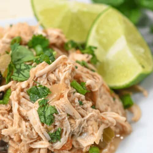 Slow Cooker Mexican Chicken, perfectly shredded with cilantro and lime slices, rests invitingly on a white plate.