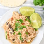 A plate of slow cooker Mexican chicken blended with black beans and cilantro, garnished with lime wedges, sits invitingly next to a warm flour tortilla.