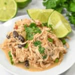 A plate of slow cooker Mexican chicken with black beans and green onions, garnished with cilantro and lime wedges.
