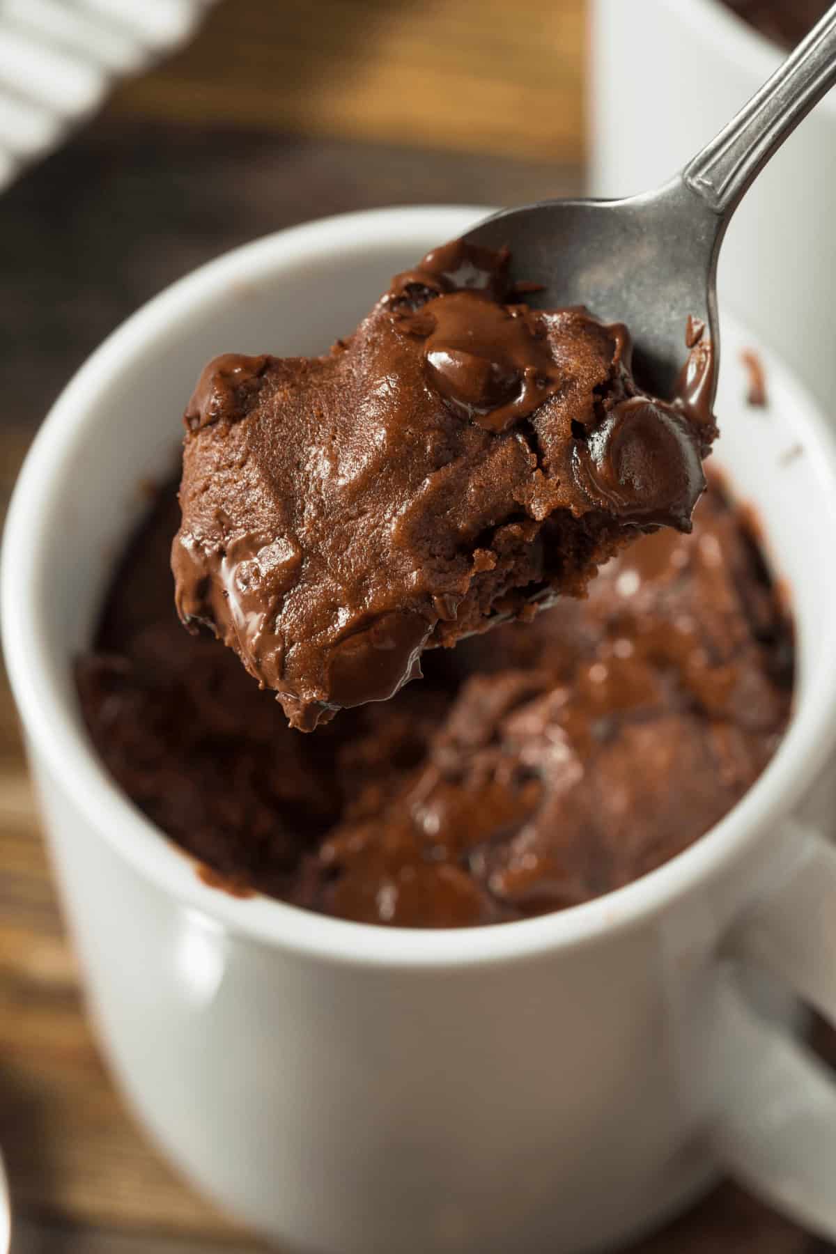 A spoonful of chocolate chip mug cake is lifted from a white mug.
