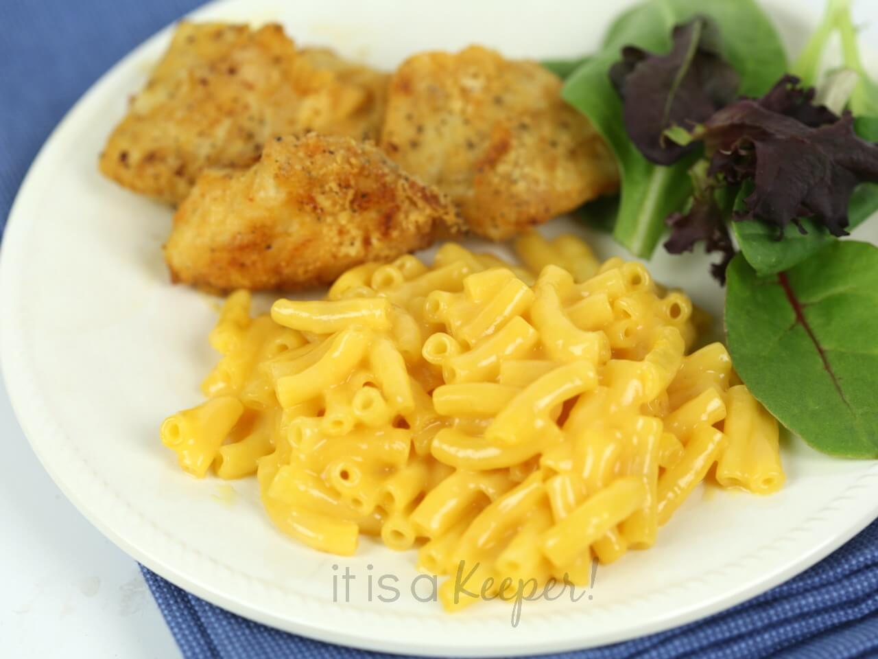 Baked Chicken Nuggets, mac and cheese, and greens on a white plate with a blue napkin. 
