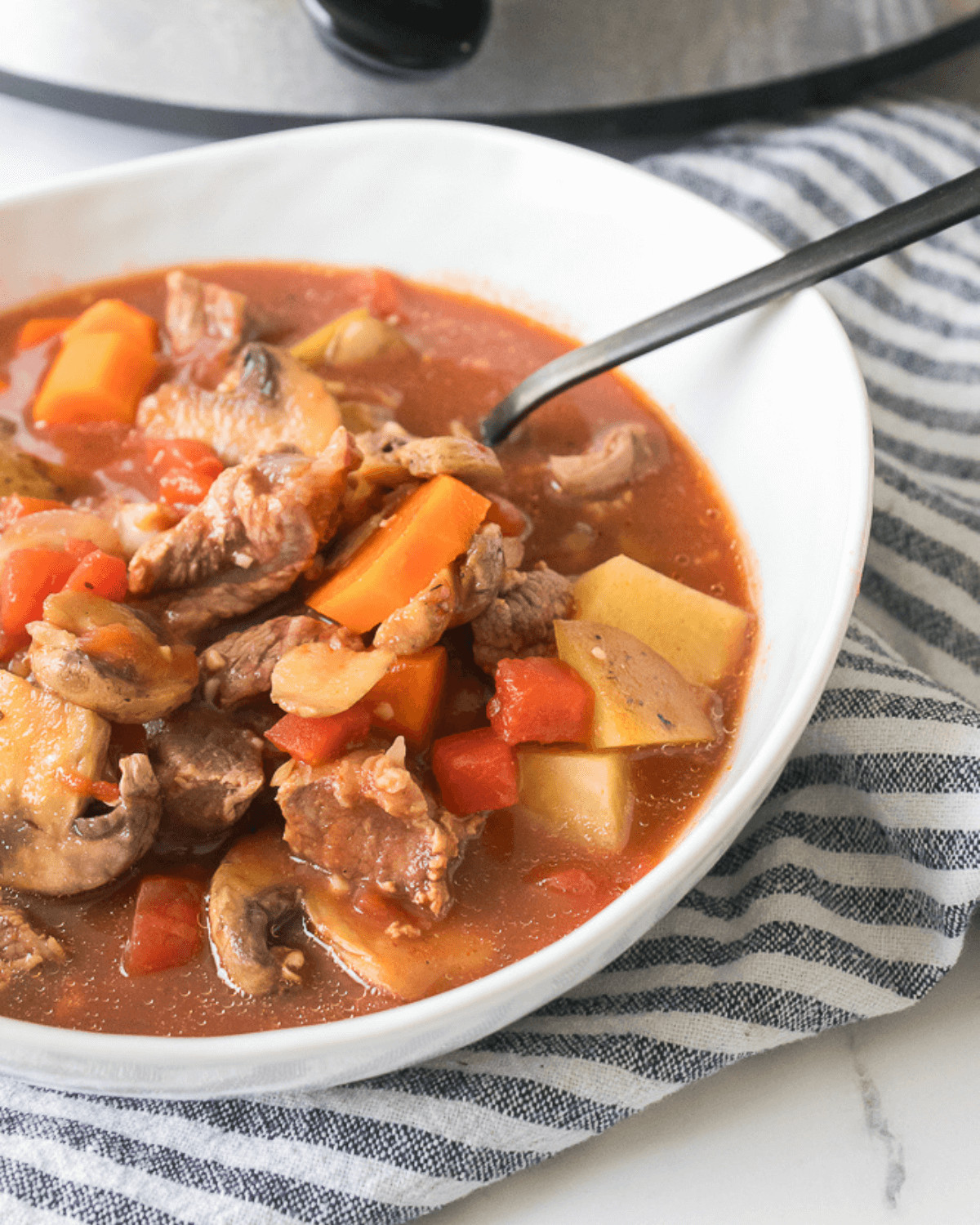 A bowl of Crock Pot beef stew in front of an instant pot.