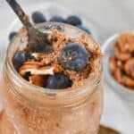 A jar of Tiramisu Overnight Oats topped with fresh blueberries and pecans, with a fork inside. A small bowl of pecans and blueberries is in the background.