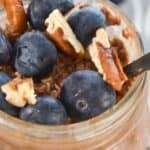 A jar with fresh blueberries and pecan pieces, with a spoon inside.