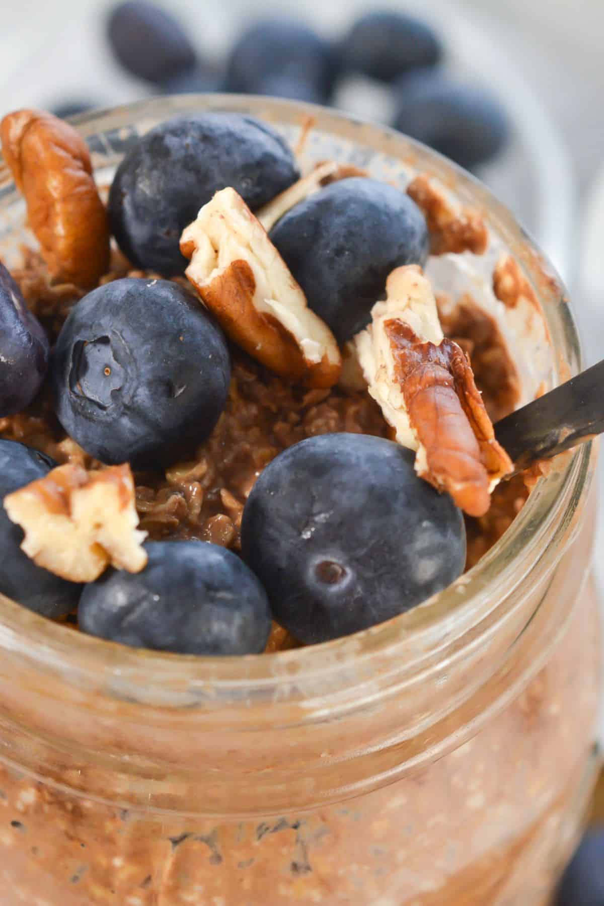 A jar with fresh blueberries and pecan pieces, with a spoon inside.