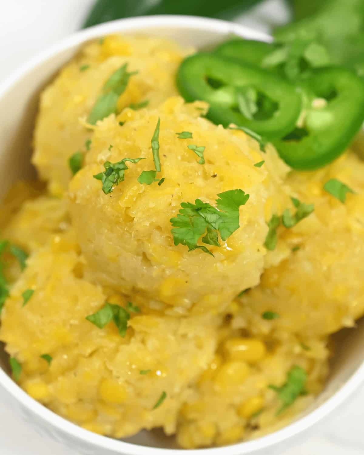A bowl of creamy corn cakes garnished with fresh parsley and sliced jalapeños, inspired by the flavors of Mexican Corn Cake.