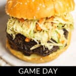 A close-up of an Asian Burger with a beef patty and slaw on a sesame seed bun. Below the burger, text reads: "GAME DAY ASIAN BURGER.