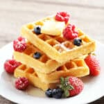A stack of three crispy waffles on a plate with raspberries and blueberries.