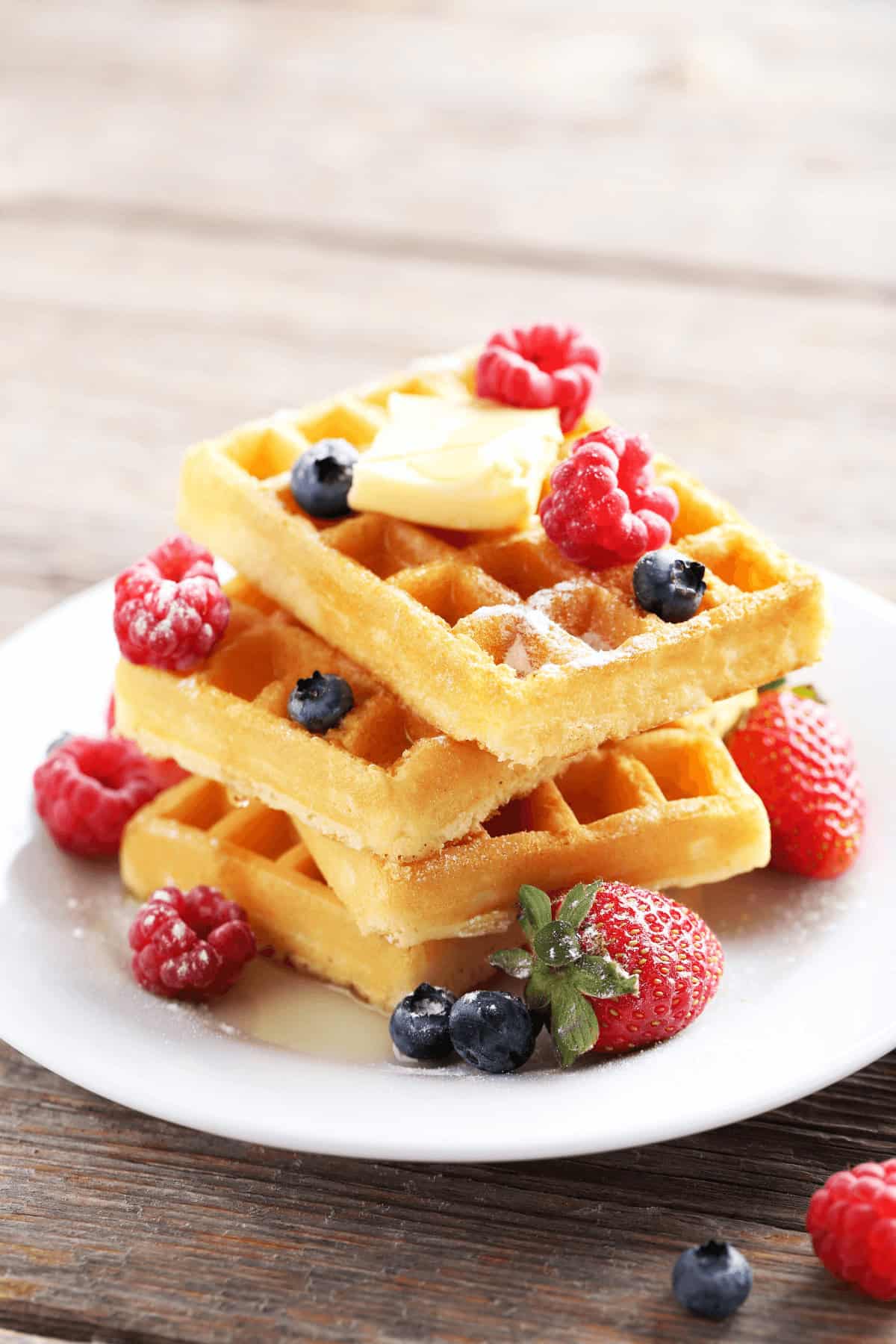 A stack of three crispy waffles on a plate with raspberries and blueberries.
