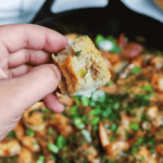 A hand holding a piece of bread in the sauce.