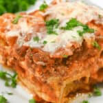 A close-up image of a slice of lazy lasagna topped with melted cheese and garnished with parsley on a white plate.