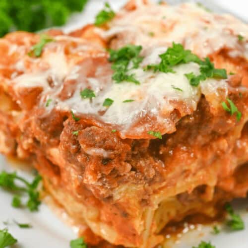 A close-up image of a slice of lazy lasagna topped with melted cheese and garnished with parsley on a white plate.