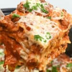 A slice of lazy lasagna being lifted from a dish, showcasing layers of pasta, cheese, and meat sauce, garnished with parsley.