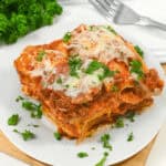 A slice of lazy lasagna topped with melted cheese and parsley, served on a square white plate with a wooden table background.