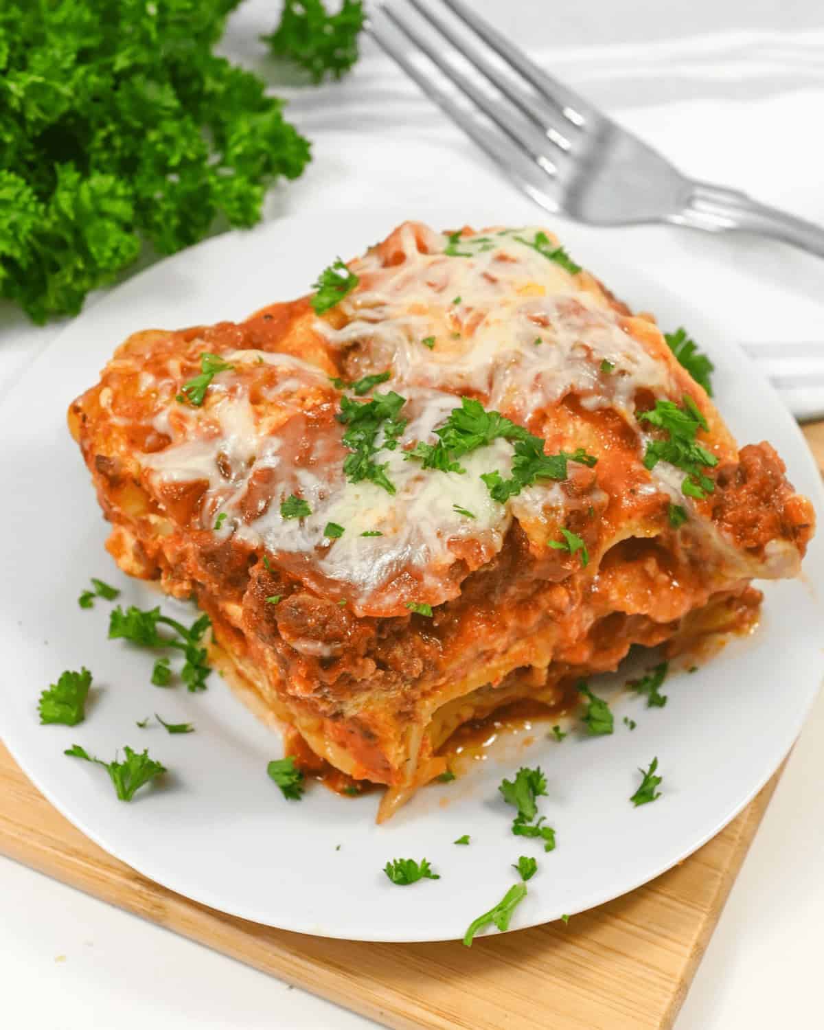 A slice of lazy lasagna topped with melted cheese and parsley, served on a square white plate with a wooden table background.