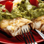 Two beef chimichangas with guacamole and tomatoes on a plate.