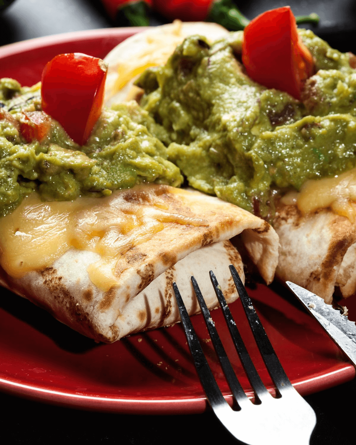 Two beef chimichangas with guacamole and tomatoes on a plate.
