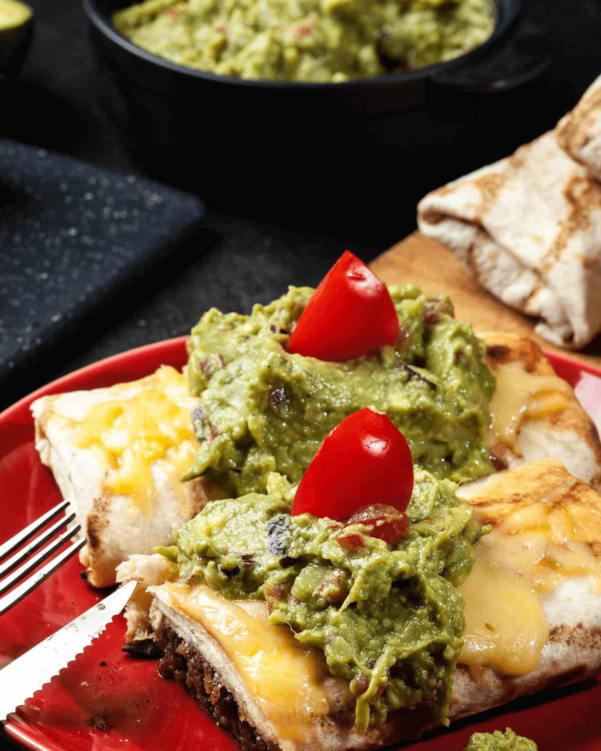 A plate of beef chimichangas served with a side of guacamole, showcased beautifully on a vibrant red plate.