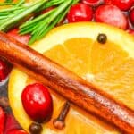 Close-up of a Christmas Simmering Pot featuring sliced orange, cranberries, cinnamon stick, rosemary, cloves, and peppercorns in liquid.