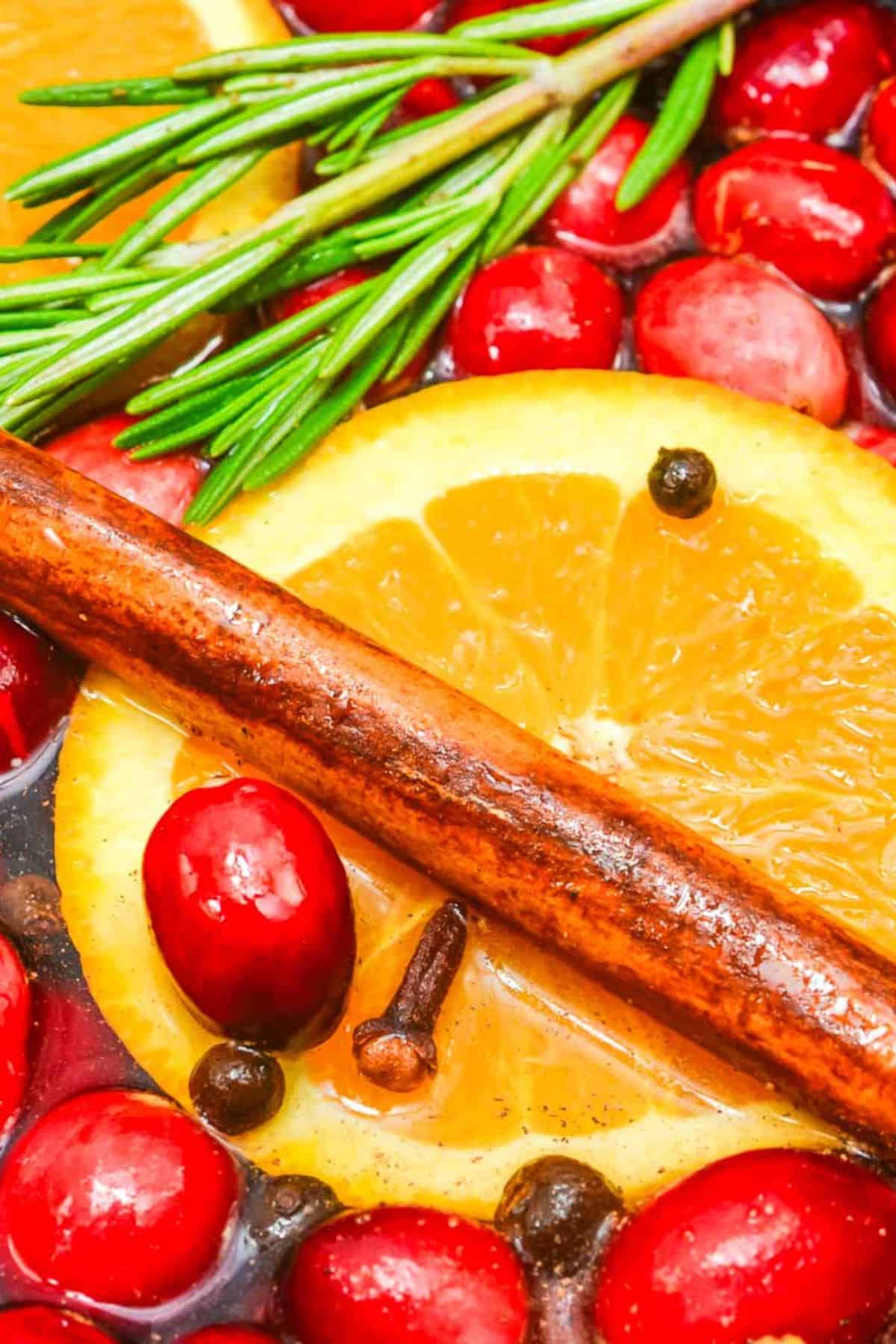 Close-up of a Christmas Simmering Pot featuring sliced orange, cranberries, cinnamon stick, rosemary, cloves, and peppercorns in liquid.
