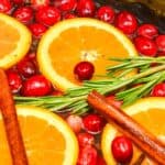 Sliced oranges, cranberries, rosemary sprigs, and cinnamon sticks float in liquid, creating a a cozy holiday potpourri.