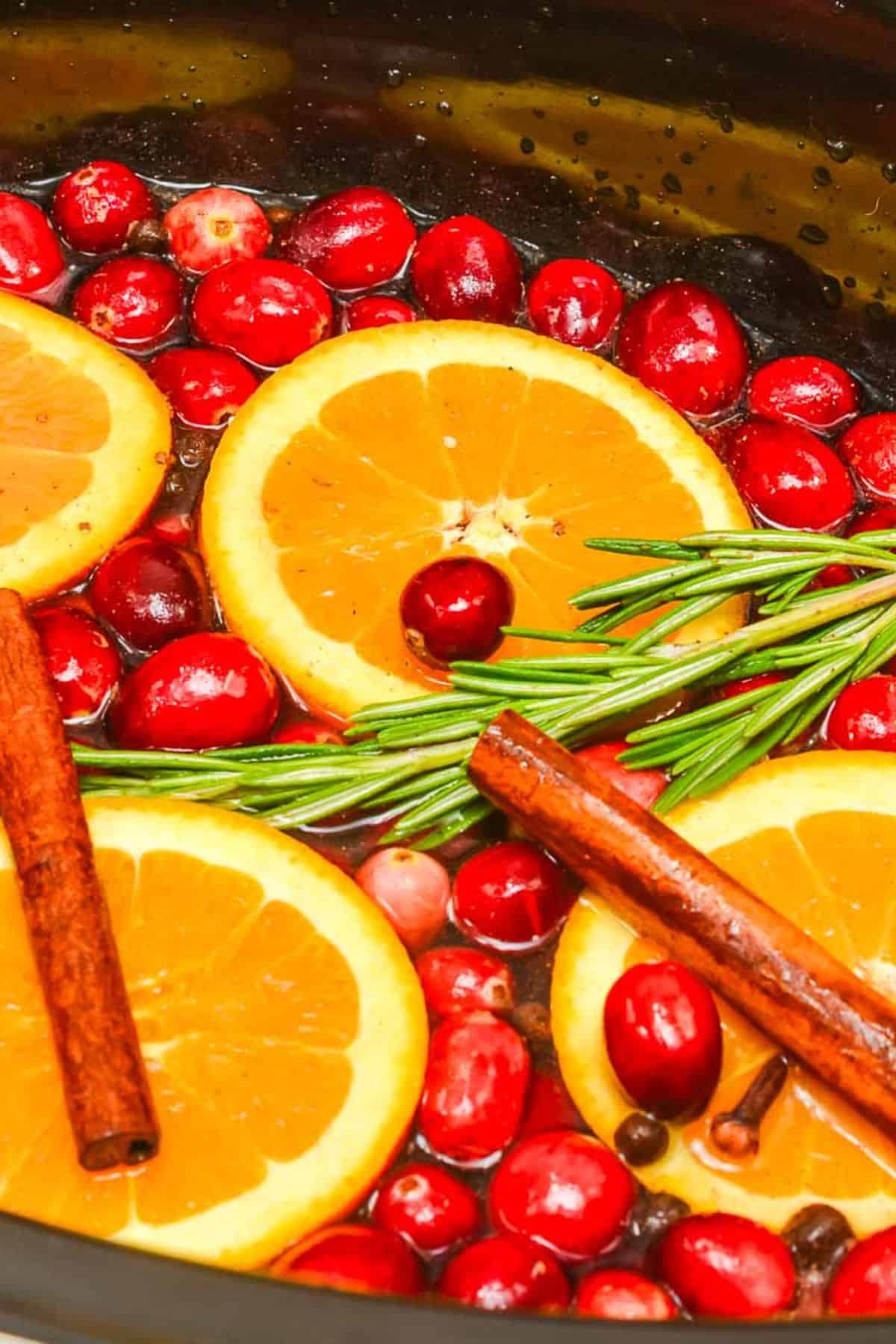 Sliced oranges, cranberries, rosemary sprigs, and cinnamon sticks float in liquid, creating a a cozy holiday potpourri.