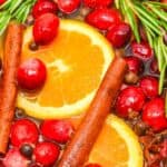 Slices of orange, fresh cranberries, cinnamon sticks, rosemary sprigs, and spices float in a festive Christmas Simmering Pot for a cozy holiday aroma.