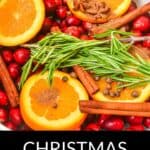 Sliced oranges, cranberries, rosemary, cinnamon sticks, spices, and herbs fill a pot labeled "Christmas Simmering Pot," creating a festive and fragrant holiday atmosphere.