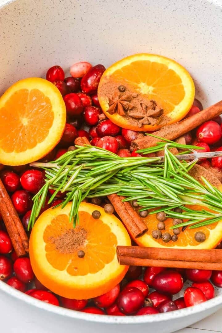 Sliced oranges, fresh cranberries, cinnamon sticks, rosemary, and spices in a white pot—everything you need for the perfect Christmas Simmering Pot, ready for cooking.