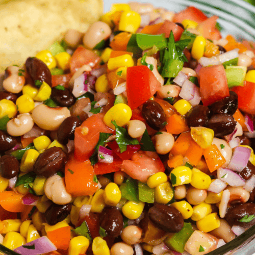 A colorful bowl of Redneck Caviar with diced tomatoes, peppers, onions, and a cilantro garnish served with tortilla chips on the side.