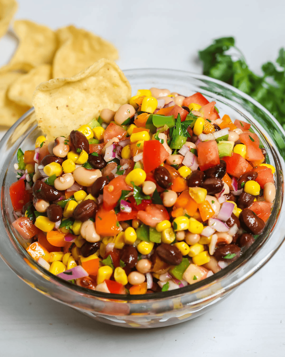 A colorful appetizer with corn, tomatoes, onions, and peppers, garnished with parsley, served with chips on the side.