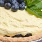 A dessert topped with a layer of garnished with fresh mint leaves sits on a creamy filling in a flaky pie crust.