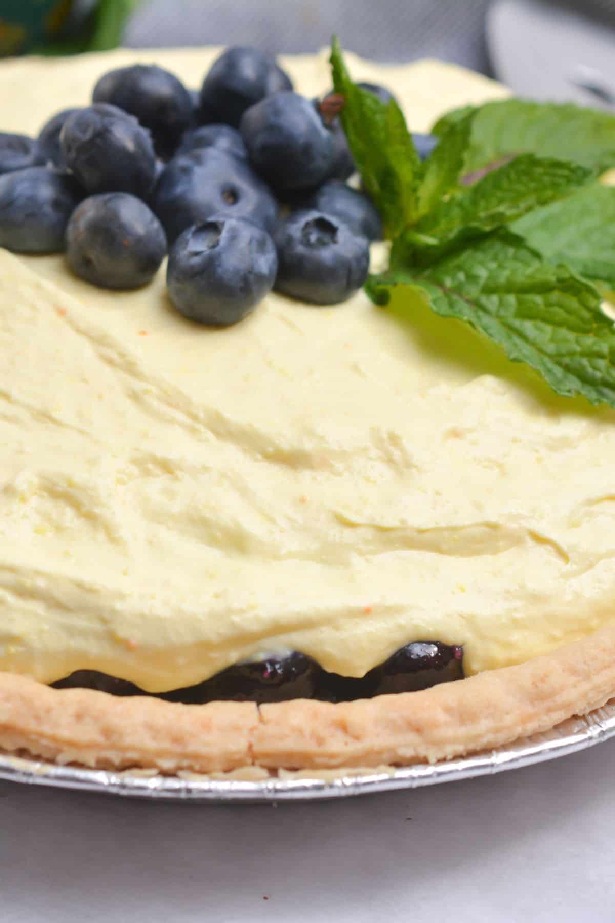 A dessert topped with a layer of garnished with fresh mint leaves sits on a creamy filling in a flaky pie crust.