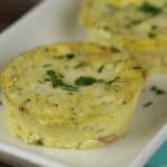 Two small ham and egg cups, garnished with chopped herbs, rest elegantly on a white rectangular plate.