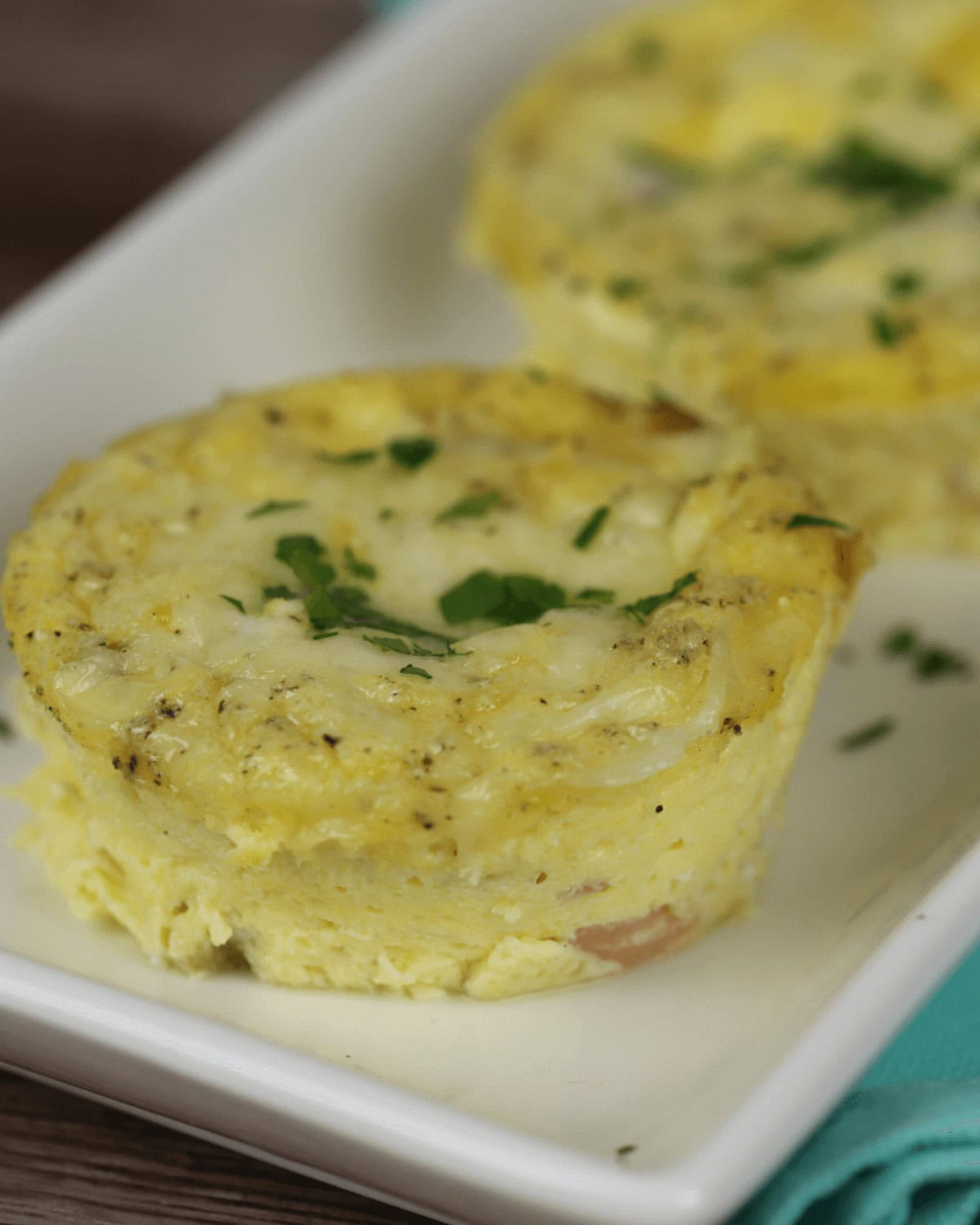 Two small ham and egg cups, garnished with chopped herbs, rest elegantly on a white rectangular plate.