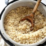 Cooked quinoa in a pot with a wooden spoon, shown in a close-up view, makes it easy to imagine how to cook quinoa in a rice cooker for perfectly fluffy results.