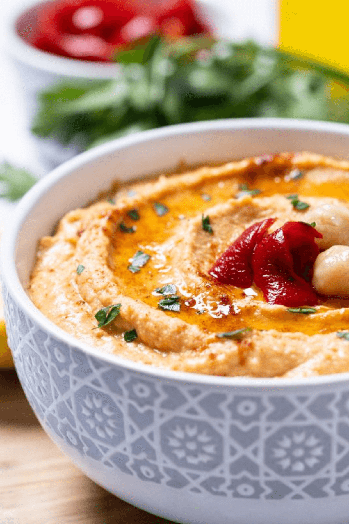 A bowl of roasted red pepper hummus garnished with herbs sits enticingly, while another bowl in the background holds vibrant red tomatoes.