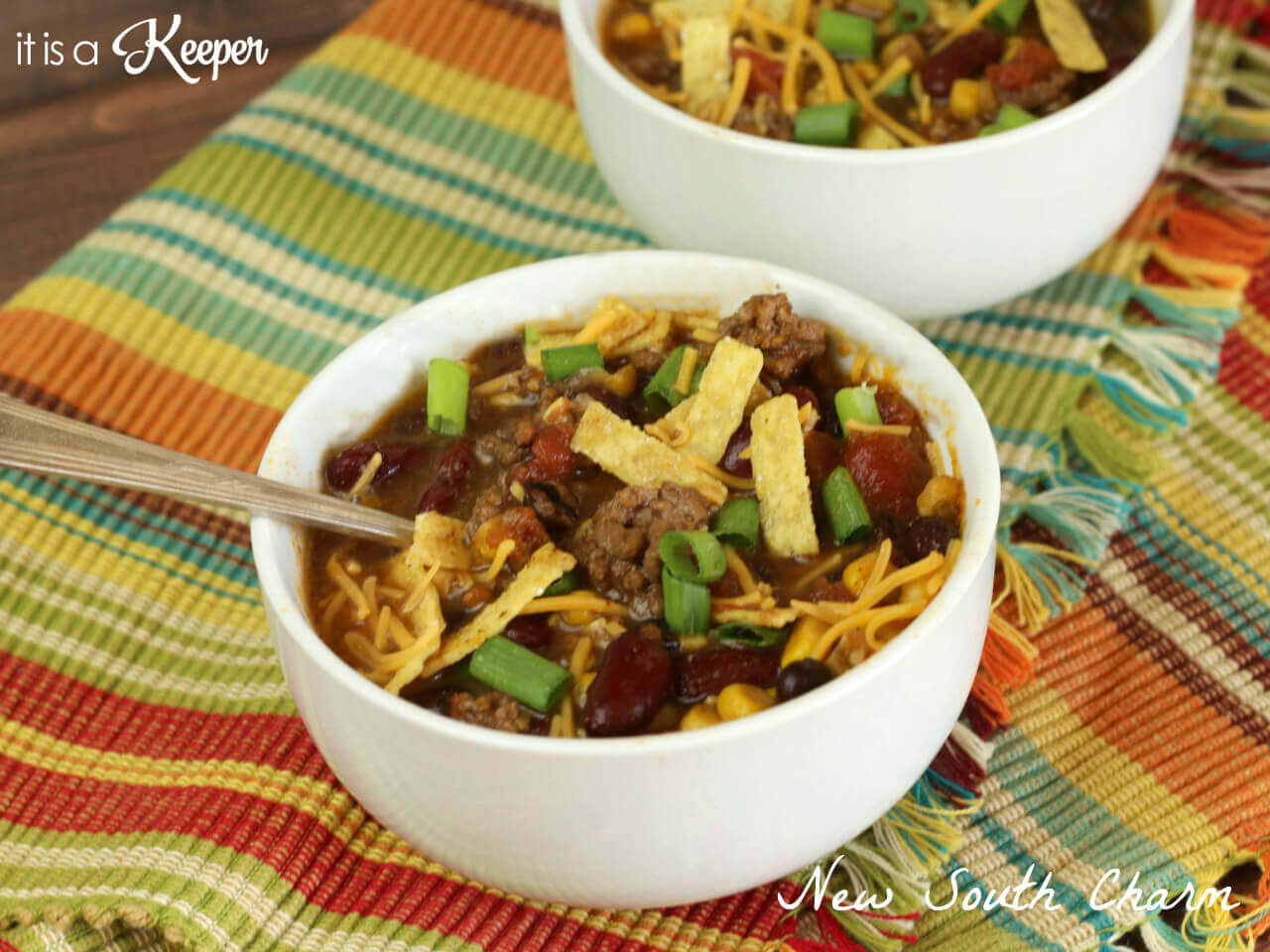 Two Slow Cooker Taco Chili in a white bowl, with a metal spoon on a multi colored place-mat. 