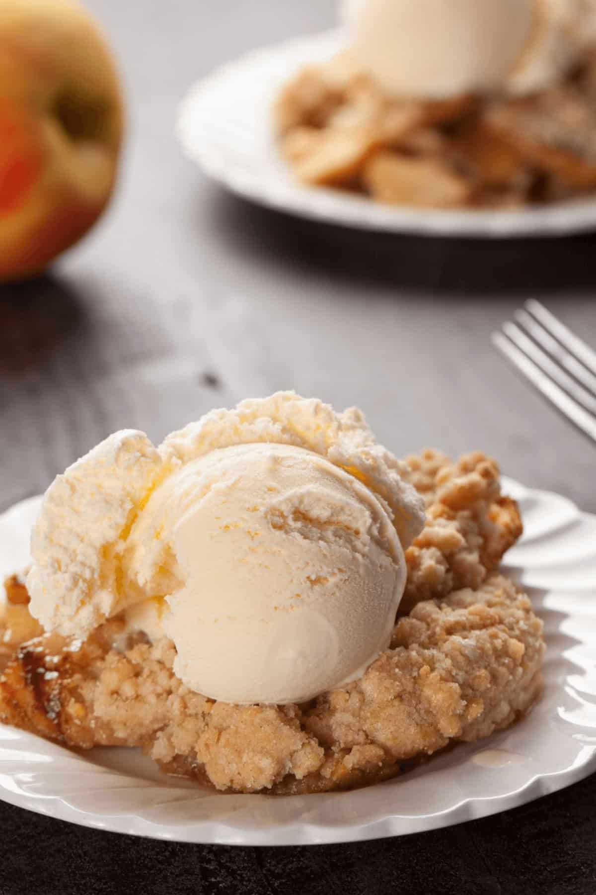 A slice of dessert topping is elegantly served on a white plate, accompanied by a scoop of vanilla ice cream. In the blurred background,
