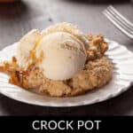A delectable apple crisp crowned with creamy vanilla ice cream graces a white plate, with "Crock Pot Apple Crisp" elegantly scripted beneath.