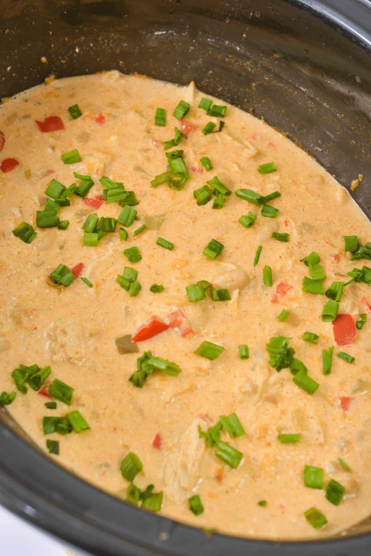 Creamy chicken stew infused with the rich flavors of cream cheese chicken chili, topped with chopped green onions and red bell peppers in a slow cooker.