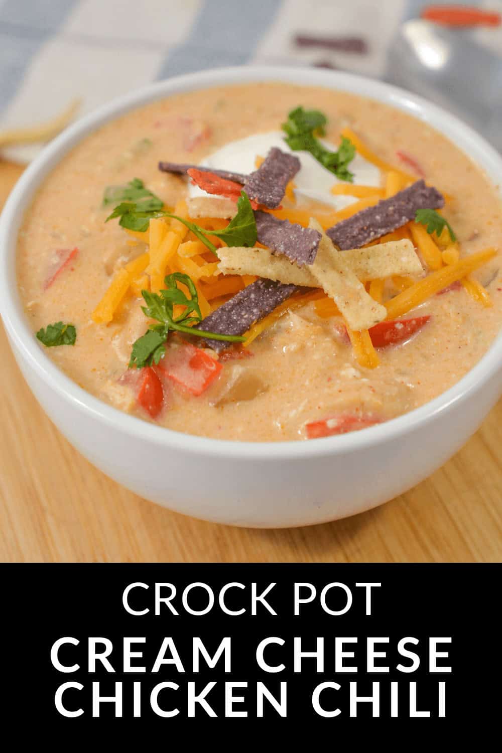 A steaming bowl of Cream Cheese Chicken Chili, adorned with shredded cheese, crispy tortilla strips, and a sprinkle of parsley.