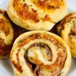A close-up of several savory Ham and Cheese Roll Ups, perfectly baked pinwheel rolls, arranged on a white plate.